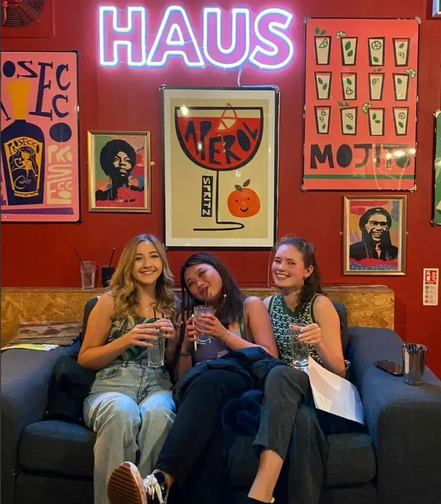3 girls part of the UOM cocktail society sitting on a sofa enjoying drinks