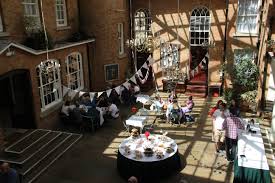 A hall with a high glass ceiling is lit by the sunlight coming through. There is bunting hanging from the ceiling, and round tables are decorated and laid out beneath for a charity event.