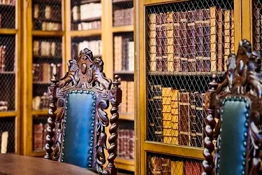 Close-up of the ornate chairs at Cosin's Library. The wood of the chair backs is carved with decoration. In the background, the book collection of the library is visible on the shelves.