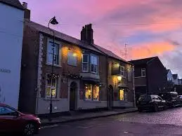A double fronted Georgian pub, Ye Old Elm Tree, is lit from within. Behind the building, the sky is pink, orange, and blue from the sunset.