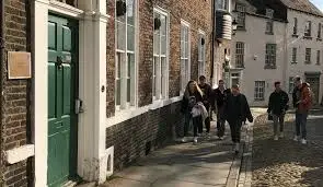 People walk along the pavement outside St Cuthbert's college on a sunny day.