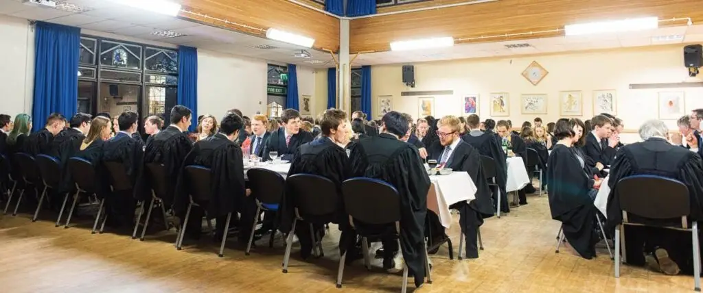 Students sit at tables laid out in long rows at a formal dinner.