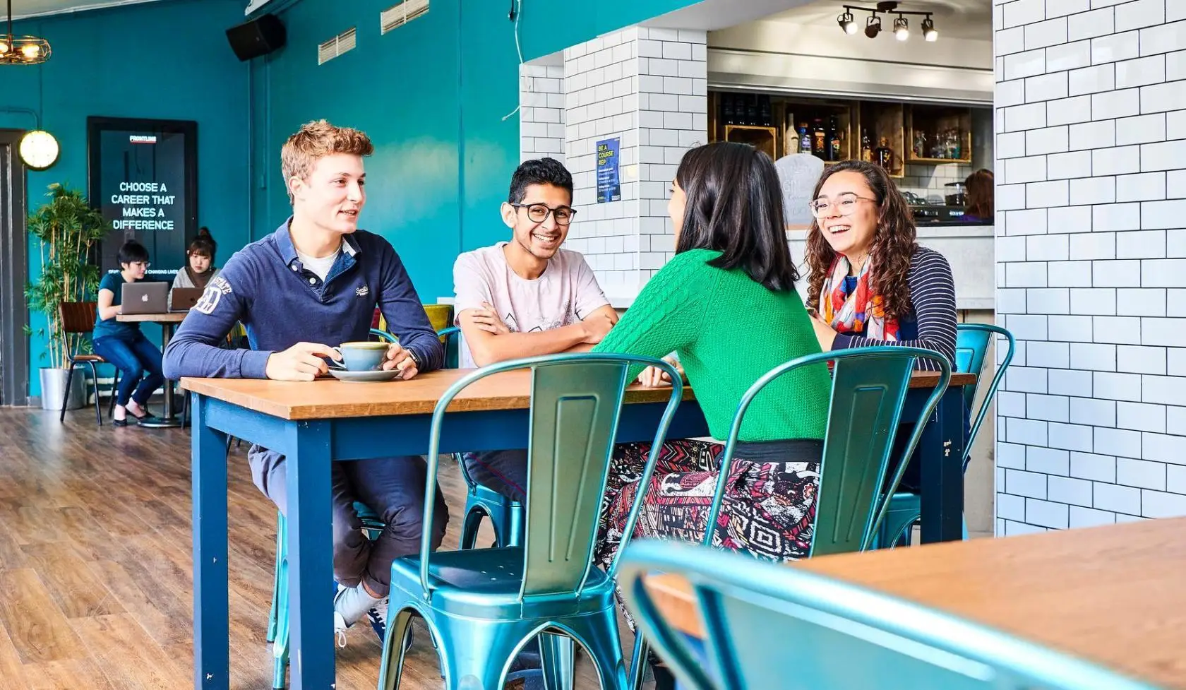 Students sit and laugh around a table, in a room with blue walls.