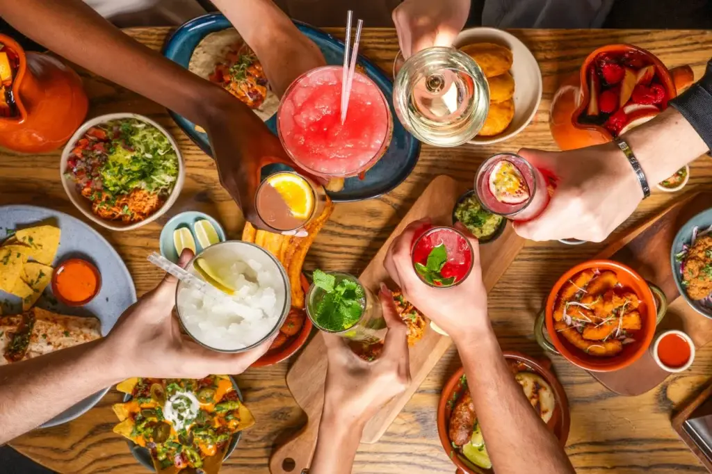 Ariel view of a table covered in Mexican food plates, with friends clinking glasses of cocktails over it
